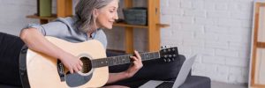woman learning to play the guitar with laptop